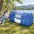 Woman reading beside the Single Door camouflage mosquito shelter in a sunny lakeside meadow