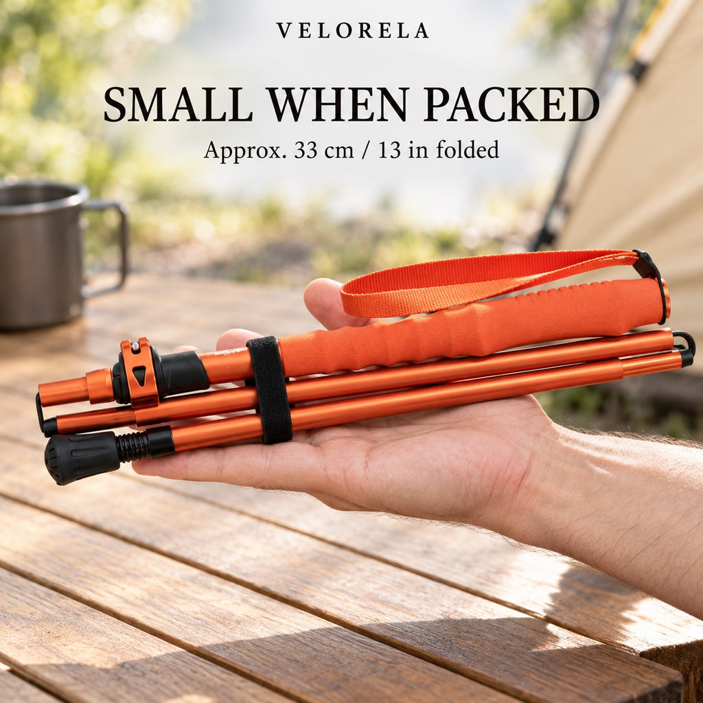 The orange five-section trekking pole folded and held across an adult hand